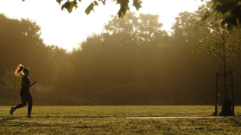 Corridore al parco all'alba — jogger su sentiero verde con luce calda del mattino